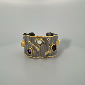 Luxury gemstone cuff bangle crafted in black rhodium plated 925 sterling silver with thick 18K gold vermeil. Featuring Green Tourmaline, Amethyst, Lemon Quartz, Smoky Quartz and Yellow Tourmaline. Adjustable statement bracelet for 16–17 cm wrists.