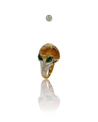 A citrine stone with green and white enamel detailing, set on a gold vermeil band, reflecting on a white surface.