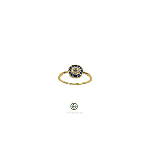 A gold-colored band ring with a round blue and white zirconia stone centerpiece, presented against a white background.