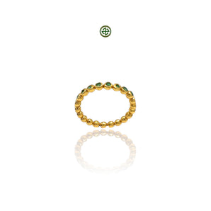 A gold-colored stacking band ring with emerald stones evenly spaced around its circumference, displayed against a white background.
