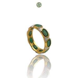 A gold-colored eternity ring with green emerald stones set in white enamel, displayed against a reflective background.
