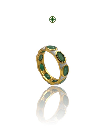 A gold-colored eternity ring with green emerald stones set in white enamel, displayed against a reflective background.