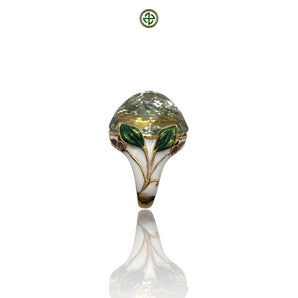 An ornate silver ring featuring a green amethyst center stone with enamel details, displayed against a white background.