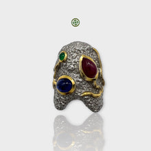 A multicolor gemstone silver ring with gold vermeil band design, featuring a central sapphire, flanked by an emerald and a ruby, set against a white background.