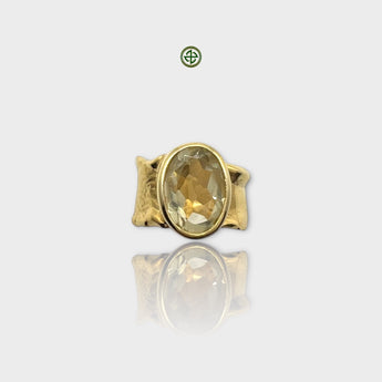 A gold-colored ring featuring an oval lemon quartz stone set in a smooth bezel, with intricate details on the band.