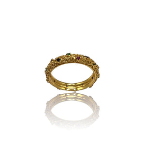 A gold-colored eternity ring with alternating ruby, emerald, and sapphire stones set in a continuous band.