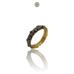 A navy blue enamel eternity ring with gold plating and inlaid with ruby, emerald, and sapphire stones, displayed on a reflective surface.