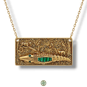 Gold-coloured rectangular necklace featuring a raised alligator with green baguette-cut stones over a detailed jungle scene, suspended from an oval-link chain.