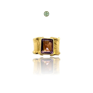 A gold-colored ring with a rectangular amethyst stone set in a smooth bezel, displayed against a white background.