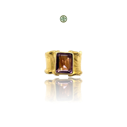 A gold-colored ring with a rectangular amethyst stone set in a smooth bezel, displayed against a white background.