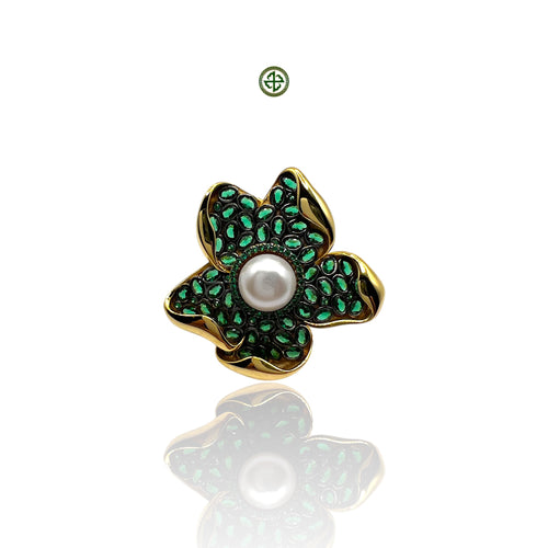 A Baroque pearl ring with a green and gold-tone band and a baroque pearl centered on a flower-like structure, against a white background.