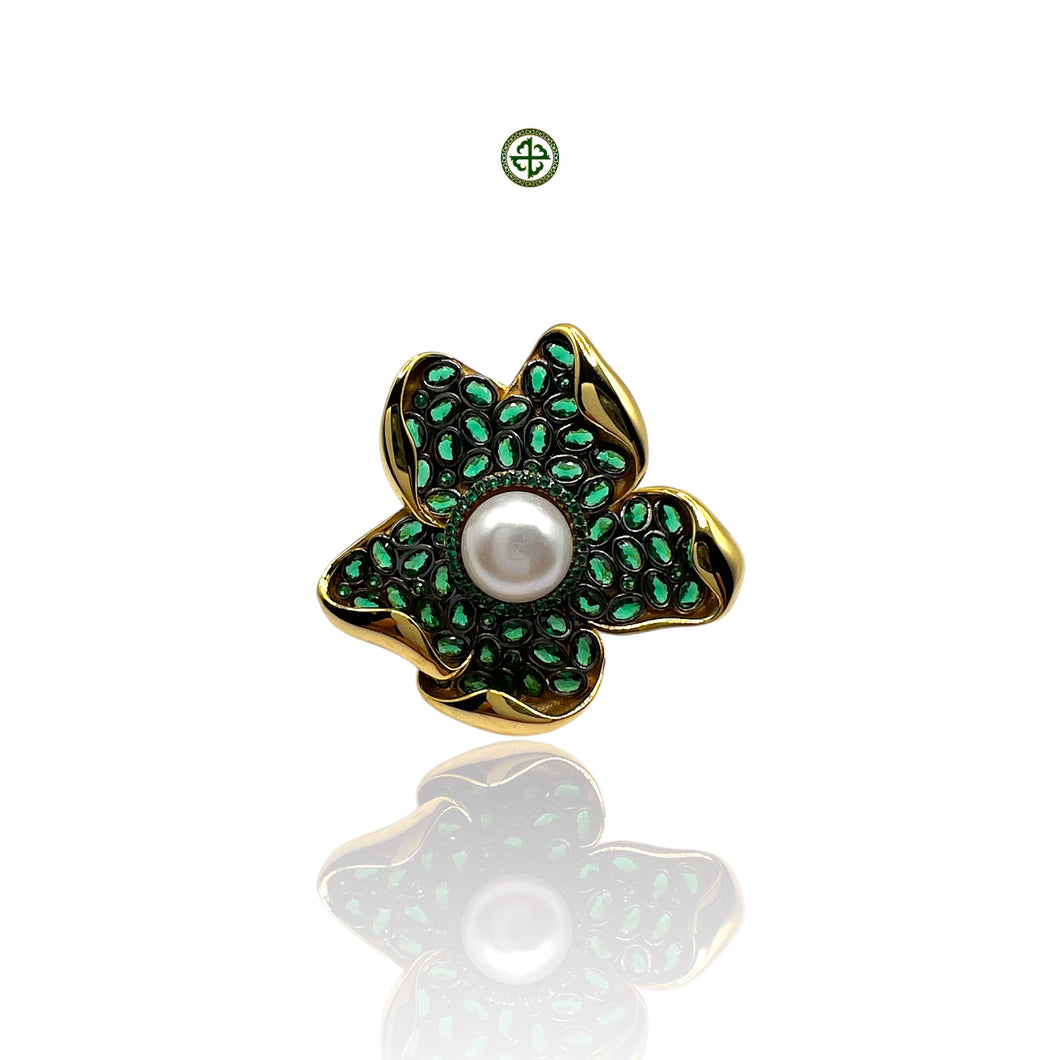 A Baroque pearl ring with a green and gold-tone band and a baroque pearl centered on a flower-like structure, against a white background.