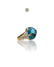 A gold vermeil ring with a large blue topaz center stone and smaller aqua marine side stones, accompanied by a turquoise, purple, and white enamel design.