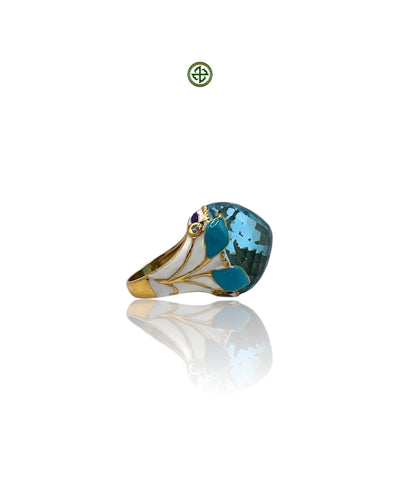 A gold vermeil ring with a large blue topaz center stone and smaller aqua marine side stones, accompanied by a turquoise, purple, and white enamel design.