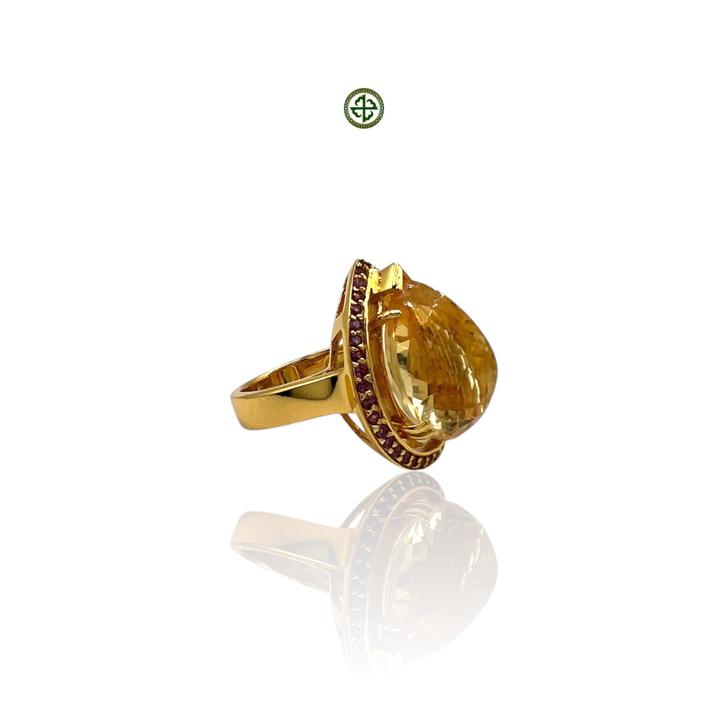A gold-colored ring featuring a large citrine stone in the center with smaller ruby stones on the sides, set on a white background.