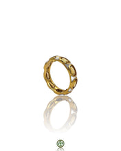 A gold-colored eternity ring with white enamel inlay and citrine stones, displayed on a reflective surface.