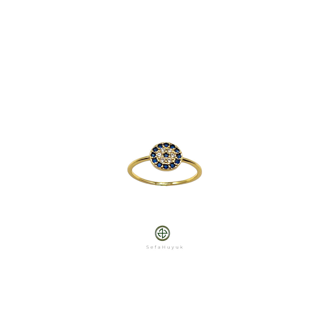 A gold-colored band ring with a round blue and white zirconia stone centerpiece, presented against a white background.