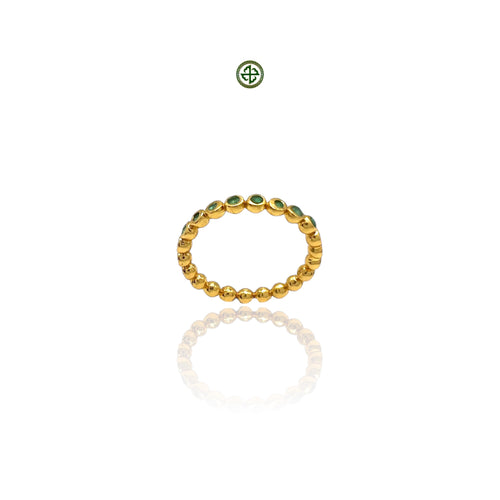 A gold-colored stacking band ring with emerald stones evenly spaced around its circumference, displayed against a white background.
