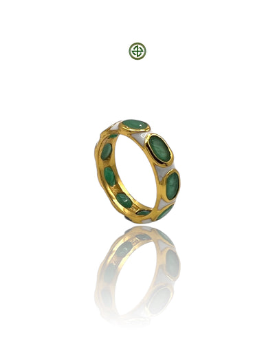 A gold-colored eternity ring with green emerald stones set in white enamel, displayed against a reflective background.