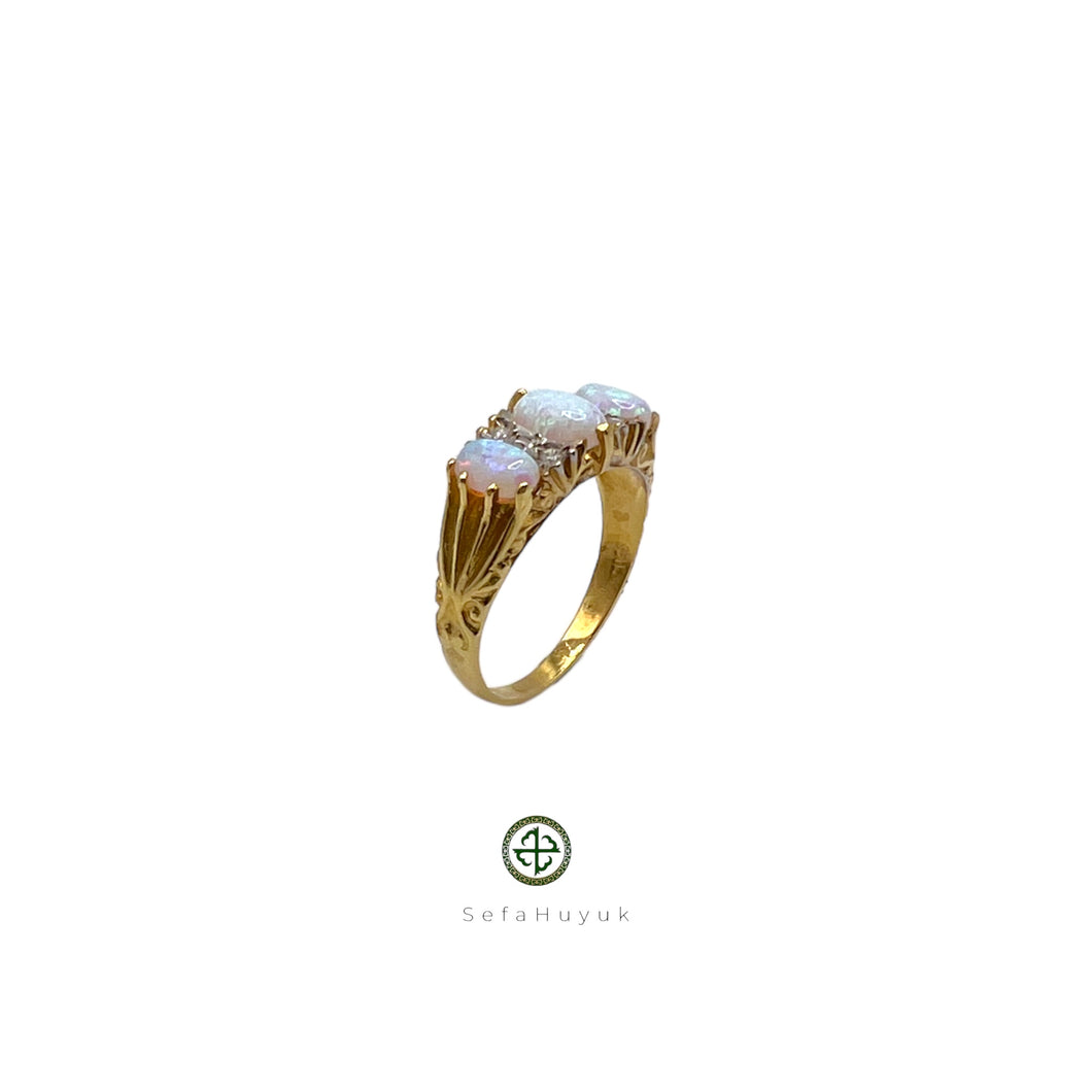 A gold-plated ring featuring an iridescent opal center stone with two additional opal inlays on the sides, set on a white background.