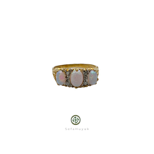 A gold-plated ring featuring an iridescent opal center stone with two additional opal inlays on the sides, set on a white background.