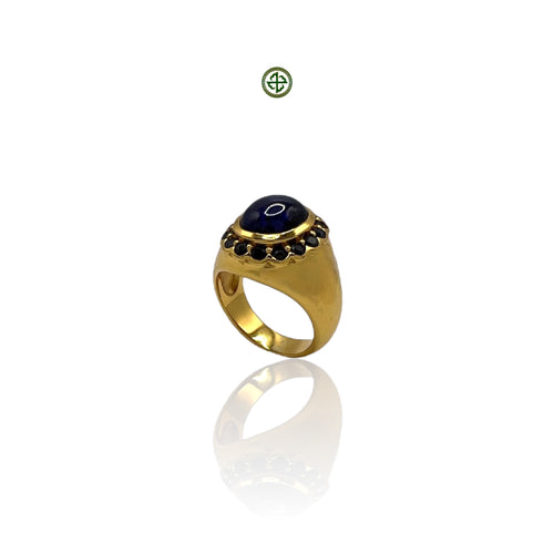 A gold-colored stacking band ring with a large blue agate center stone and smaller star sapphire side stones, set on a white background.
