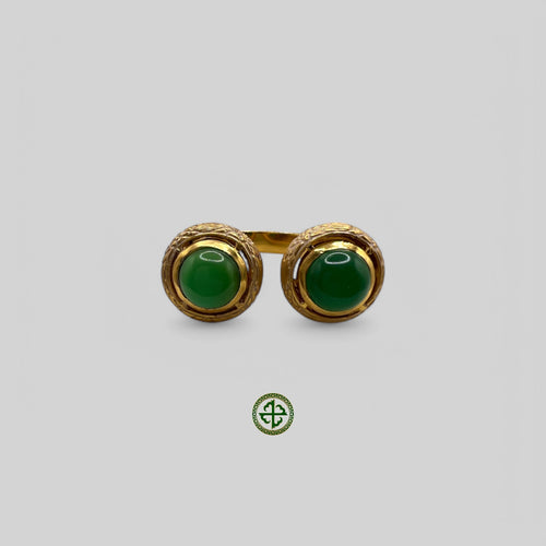 A gold-colored ring featuring two green agate gemstones with white enamel detailing, presented against a white background.