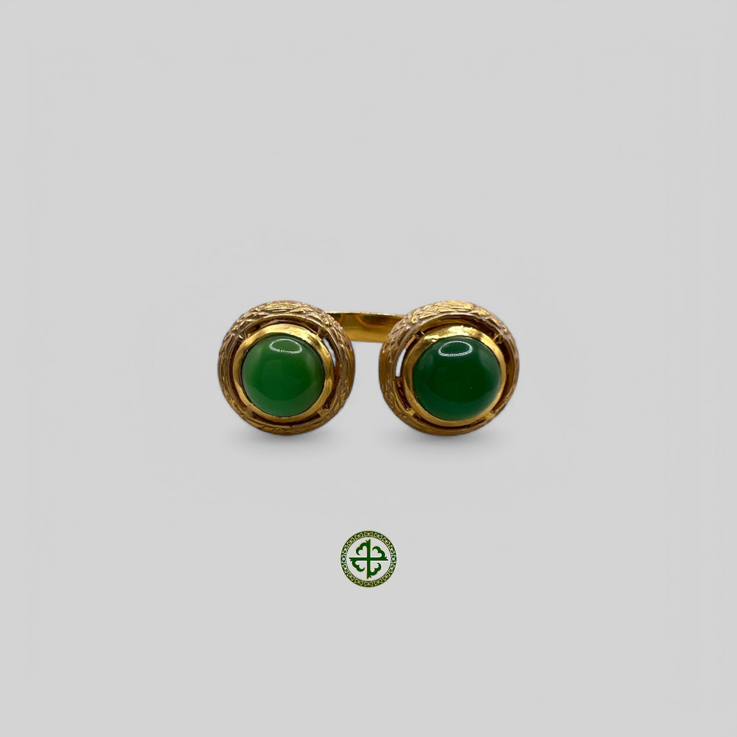 A gold-colored ring featuring two green agate gemstones with white enamel detailing, presented against a white background.