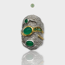 A silver ring with a large green onyx center stone, flanked by smaller green stones, with intricate textures and gold vermeil details.