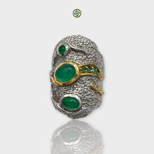 A silver ring with a large green onyx center stone, flanked by smaller green stones, with intricate textures and gold vermeil details.