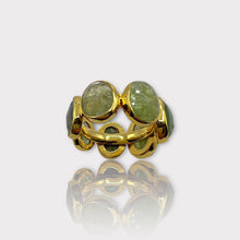 A gold-colored eternity ring with green tourmaline stones set in a silver band, viewed from the side.