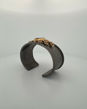 Luxury cuff bangle crafted in black rhodium plated 925 sterling silver with thick 18K gold vermeil. Featuring a marquise green amethyst centerpiece surrounded by garnet gemstones. Adjustable statement bracelet for 16–17 cm wrists.
