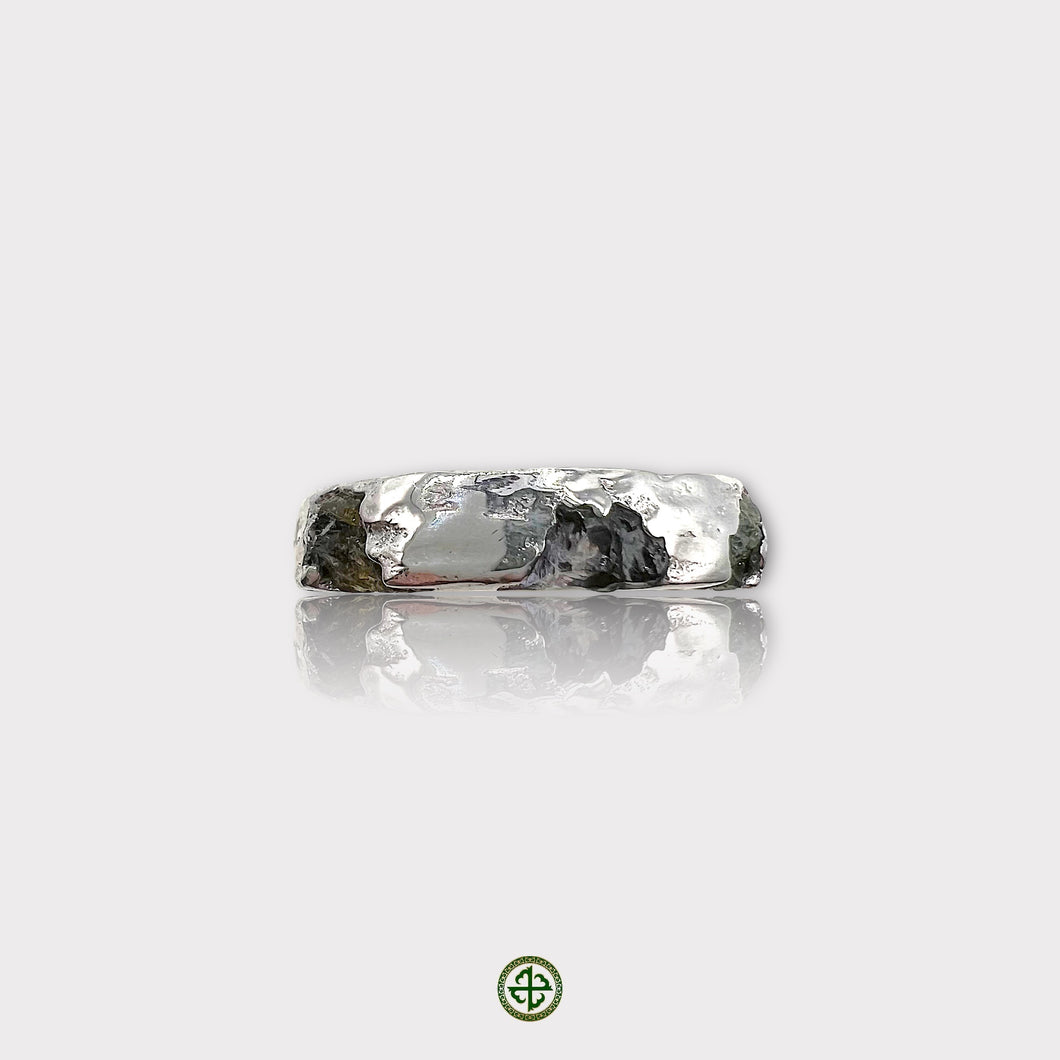 A silver band ring featuring a raw black tourmaline and raw peridot gemstone set