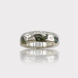 A silver band ring featuring a raw, uncut peridot gemstone with a textured finish.