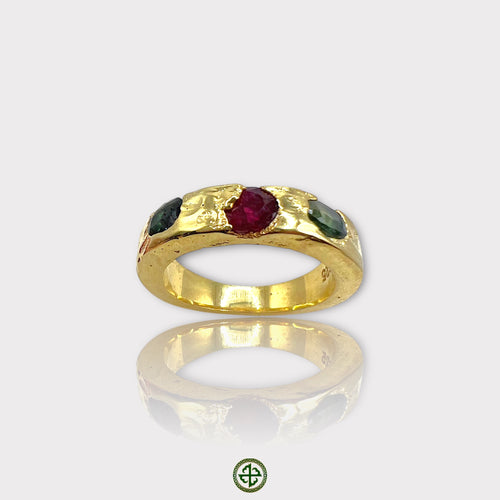 A gold-colored band ring featuring a central ruby with green tourmaline on either side, set in a textured setting.