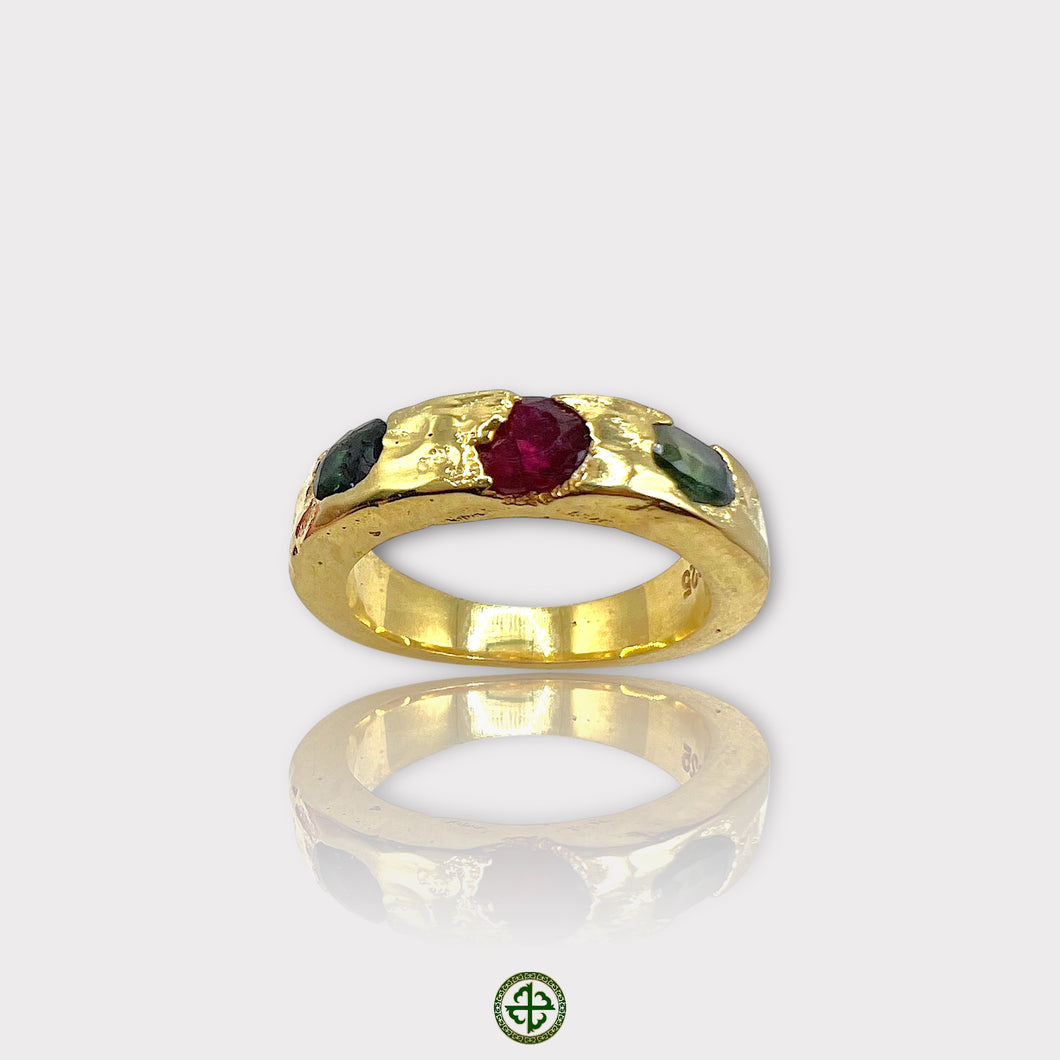 A gold-colored band ring featuring a central ruby with green tourmaline on either side, set in a textured setting.