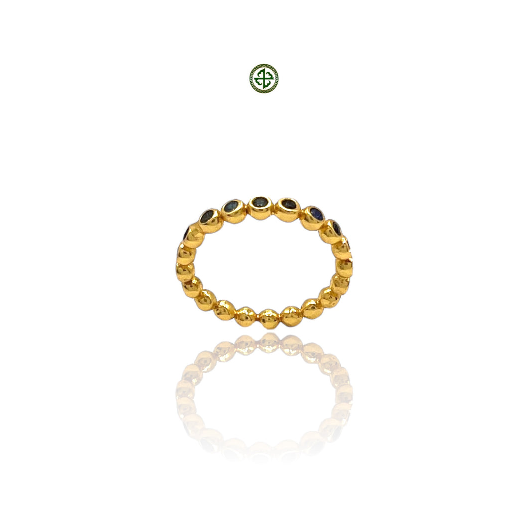 A gold-colored stacking band ring with sapphire stones set in a pattern around its circumference.