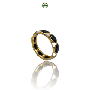 A gold-colored eternity ring with blue sapphire stones and white enamel inlay, displayed on a reflective surface.