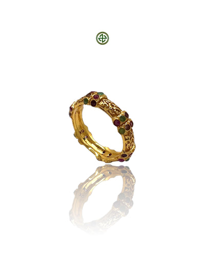 A gold-colored eternity ring with ruby, emerald, and amethyst stones set around its circumference on a white background.