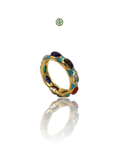 A gold-colored eternity ring with multiple colorful gemstones and turquoise enamel detailing, displayed against a reflective background.