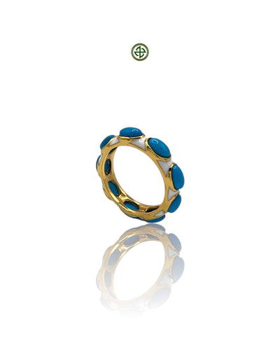 A gold-colored eternity ring with white enamel and turquoise inlays, displayed on a reflective surface.